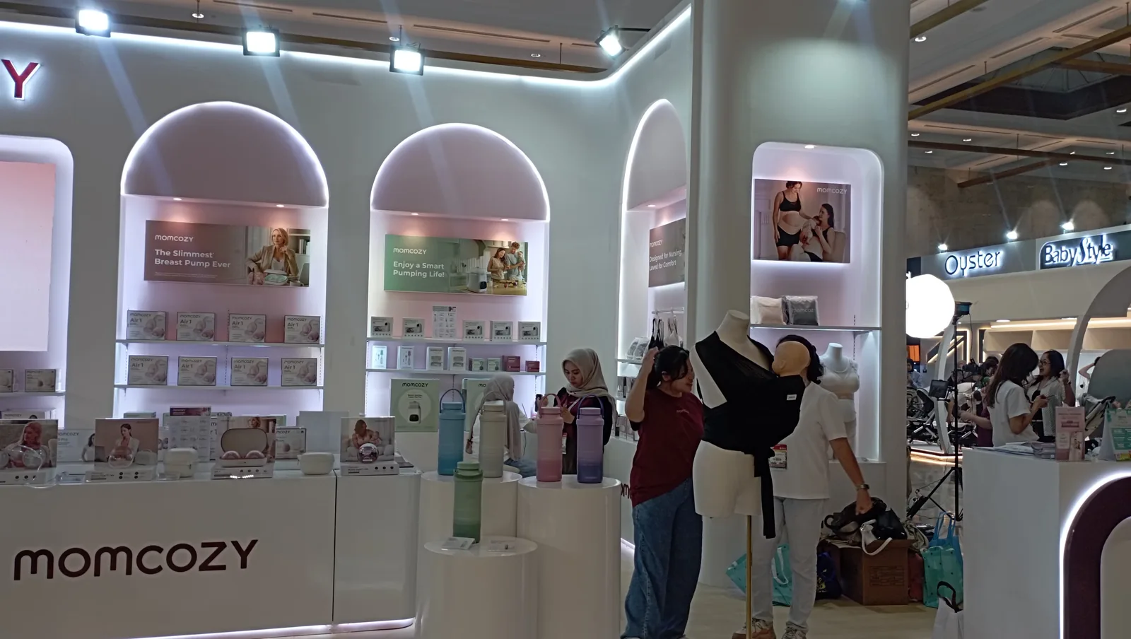 Rak lengkung bercahaya dan pengunjung di booth Momcozy.